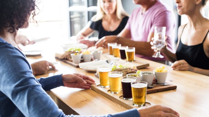 A woman adjusting her flight of craft beers while sitting at a table with friends │ craft beer in Albuquerque