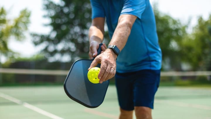 A man holding a pickleball paddle and ball as he