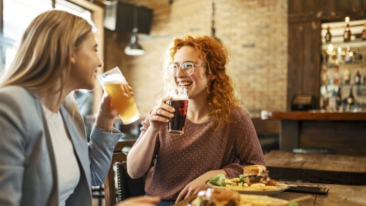 two smiling women drinking a pint of beer over dinner | pubs in Santa Fe