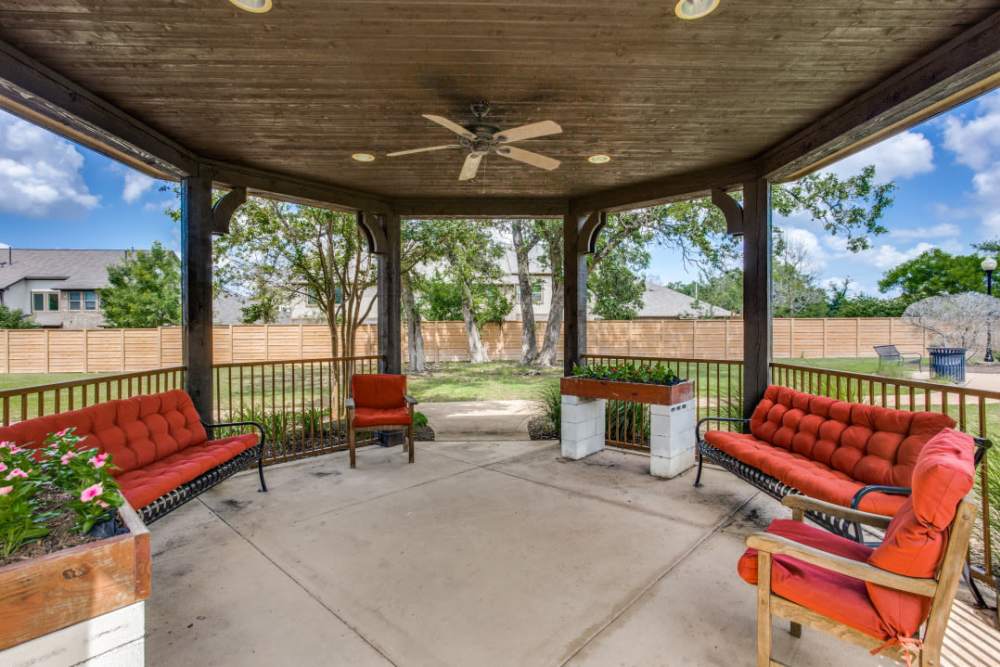 Covered patio at Isle at Cedar Ridge in Cedar Park, Texas, with red chairs and a ceiling fan under a gazebo.