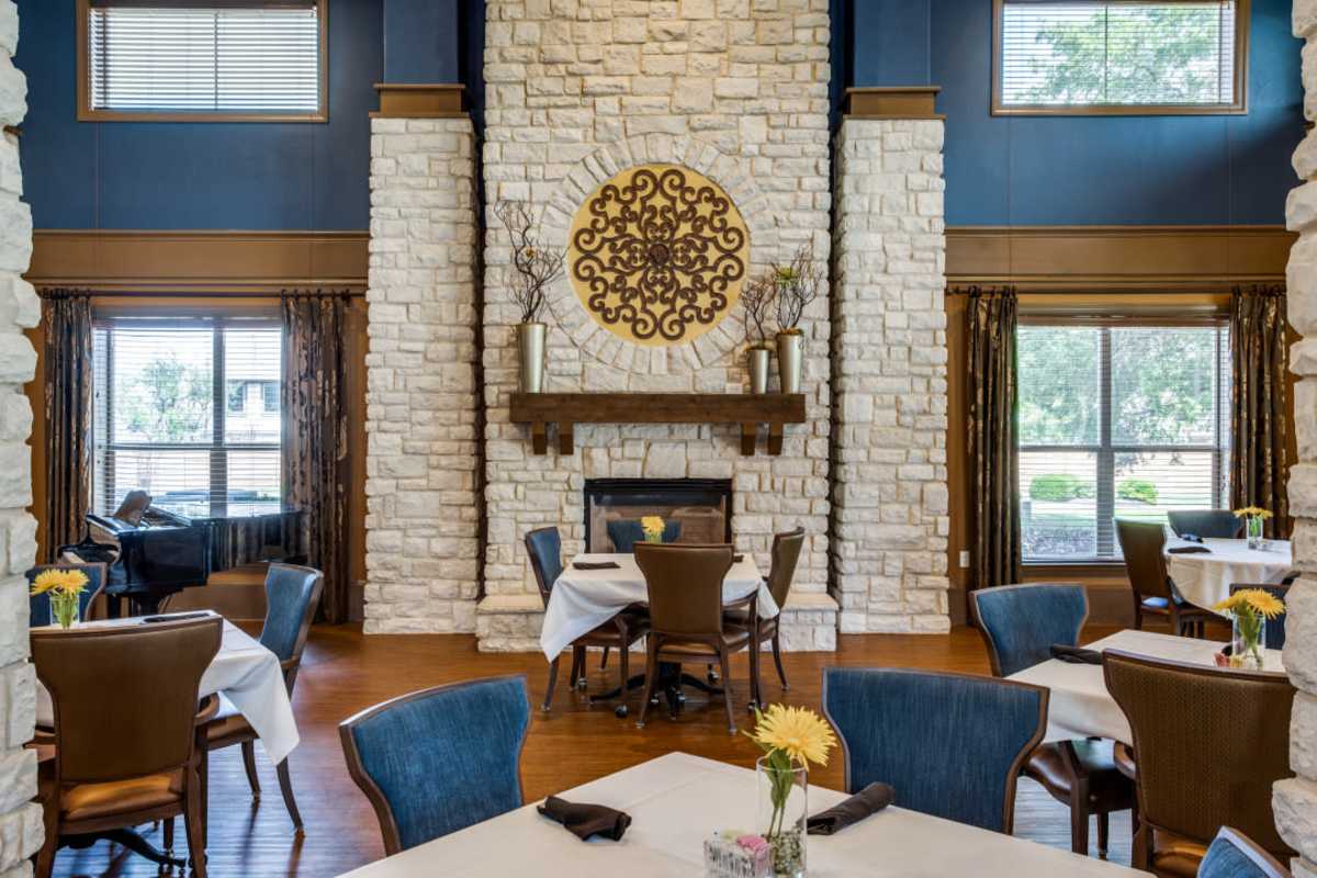 Dining room at Isle at Cedar Ridge in Cedar Park, Texas, with warm tones, large windows, and tree views outside.