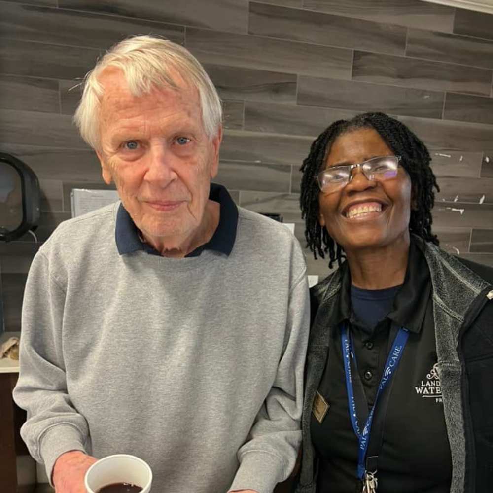 Smiling caregiver and resident sharing a moment over coffee, showing compassionate memory care at Watermere Frisco.