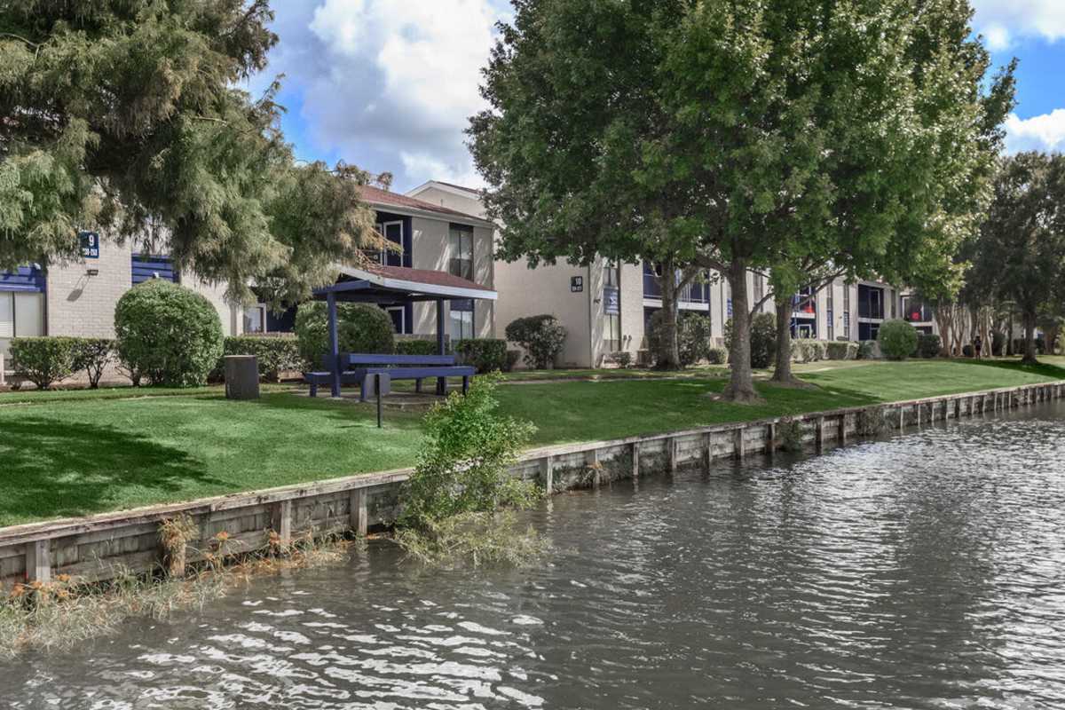 Exterior view of the apartments, calm waterway, shaded picnic area, and trimmed greenery at The Breakers in Texas City, Texas