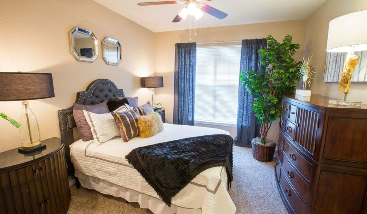 Well-lit bedroom with comfortable bed, large window, plush carpet, ceiling fan and other furniture items at Cobblestone Park in Manvel, Texas 