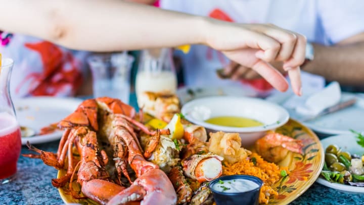 Closeup of a plate of lobster and seafood with hand reaching for butter | seafood restaurants in Jacksonville