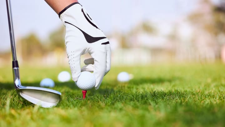 A gloved hand places a golf ball on a tee at a golf course