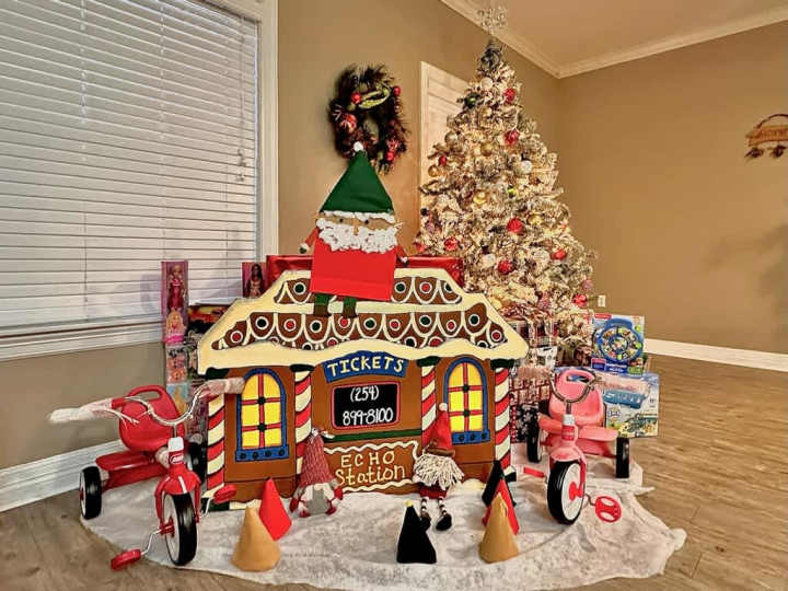 A box decorated to look like a train station for gnomes with a Christmas tree in the background.