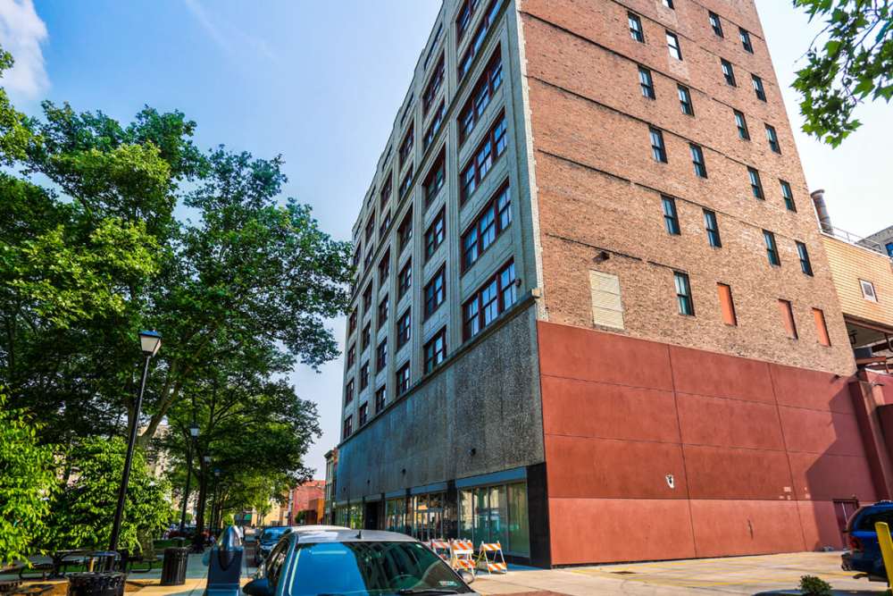 Modern apartment building with large windows and surrounding greenery, featuring a gated entrance and outdoor seating areas at Stone Center Lofts in Wheeling, West Virginia
