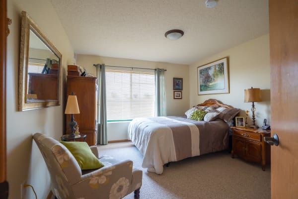 Resident bedroom with bed, dresser, chair and large windows at Meadows on Fairview in Wyoming, Minnesota