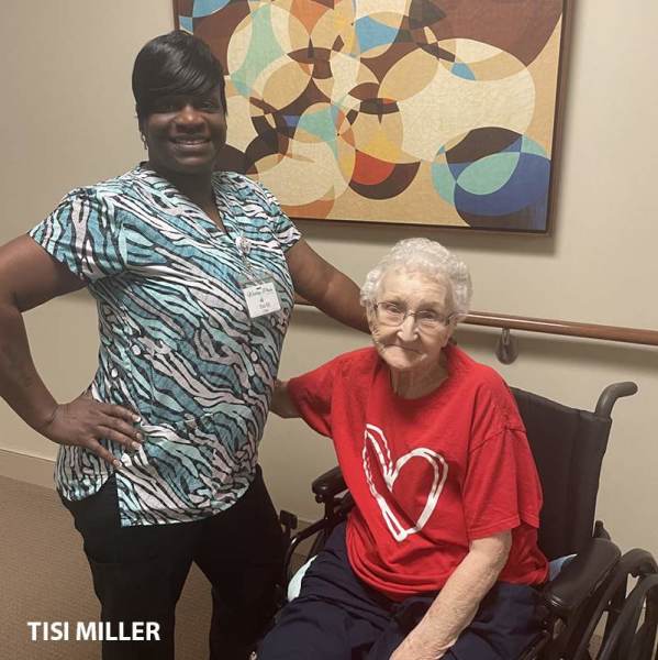Caregiver Tisi standing behind resident seated in a wheelchair