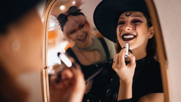 A person dressed as a witch smiling in the mirror applying lipstick | DIY Halloween costume ideas