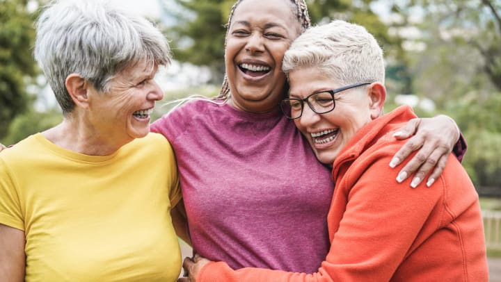 Three older women hugging and laughing.