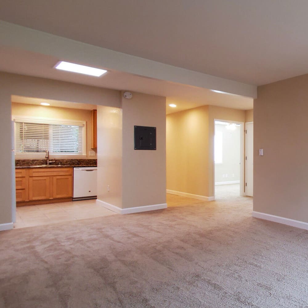 Living room with plush carpet and a view of kitchen with white appliances at Mission Rock at Marin in San Rafael, California