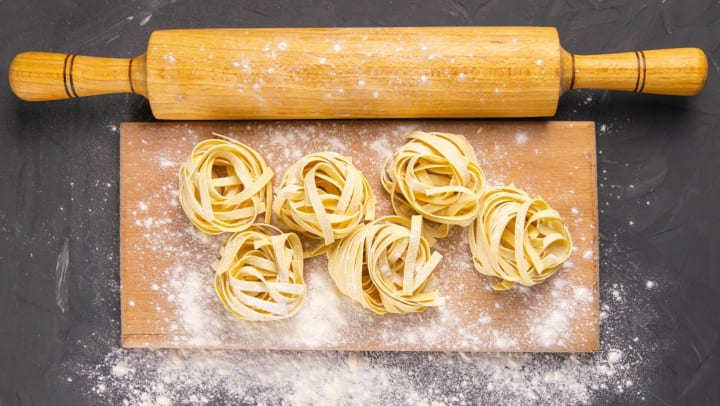 Aerial view of uncooked fresh pasta noodles on a wooden board with a rolling pin on a dark slate backgroud