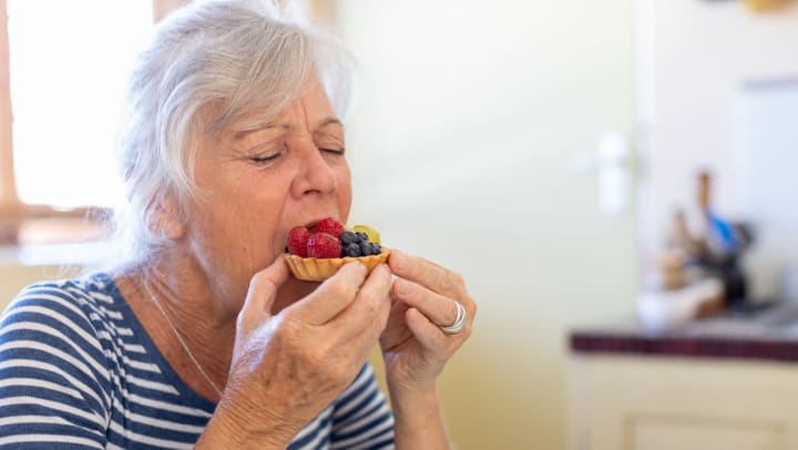 Older woman eating a small fruit tart