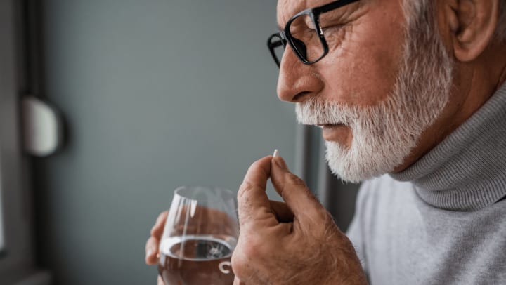 Senior man holding a glass of water taking medication
