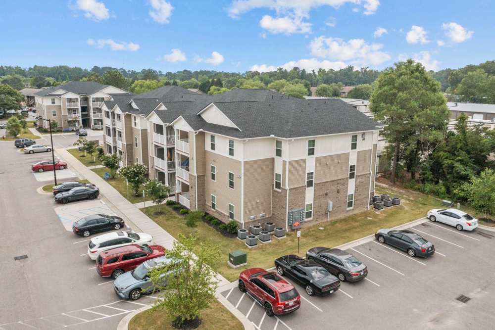 Apartment community with three-story buildings, ample parking, and green landscaping in a tranquil setting at Old Firetower Place in Greenville, North Carolina