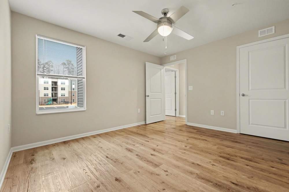 Empty bedroom with wood-style flooring and ceiling fan, featuring a window overlooking the community pool at Leonard Greene in Dallas, North Carolina