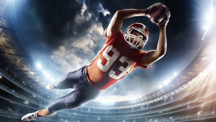 A football player in an orange jersey and gray pants making a diving catch.