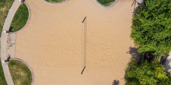 Aerial view of a sand volleyball court with net bordered by trees and pathways at The Domain at Columbia in Columbia, Missouri