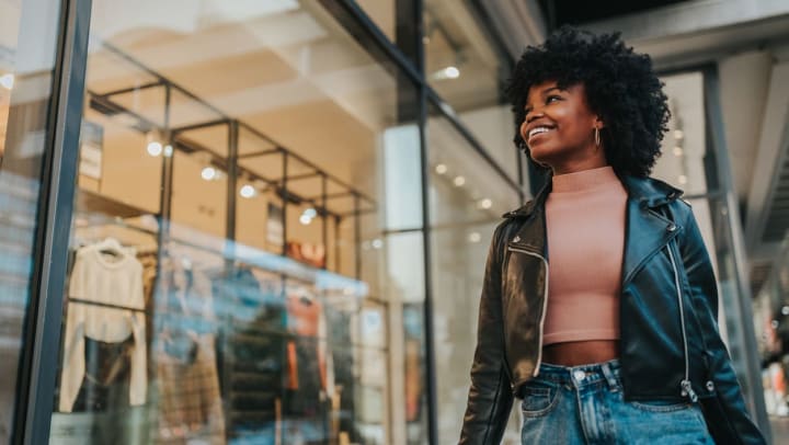 Woman window shopping and looking inside clothing store while smiling