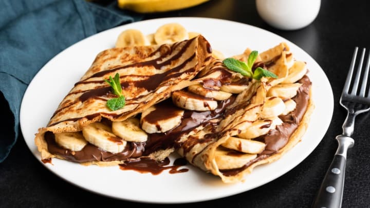Close-up of a white dish with a Nutella and banana-filled crepe | Crepes Near Irving
