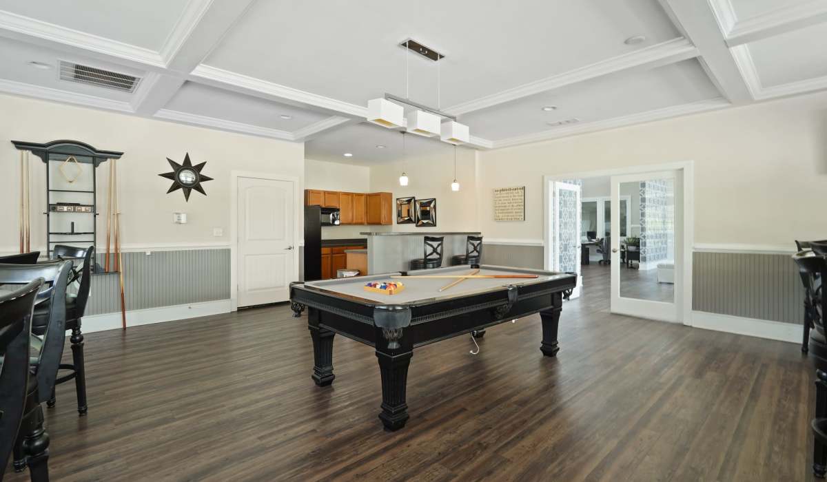  Game room featuring a billiard table with cues and balls, surrounded by wooden flooring, bar stools, and kitchen area at Village at Rice Hope in Port Wentworth, Georgia