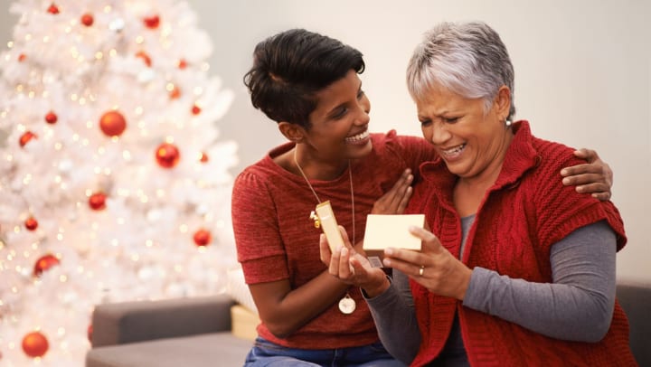 An older woman receiving a holiday present from her adult daughter.