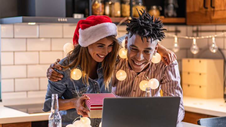 Smiling couple in a kitchen looking at a computer screen while smiling and holding a gif