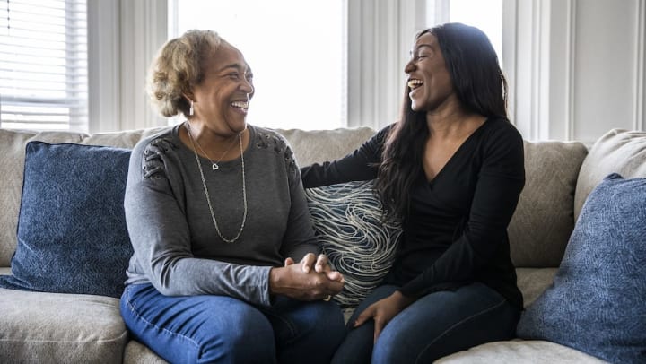 Senior mother and adult daughter laughing on a sofa