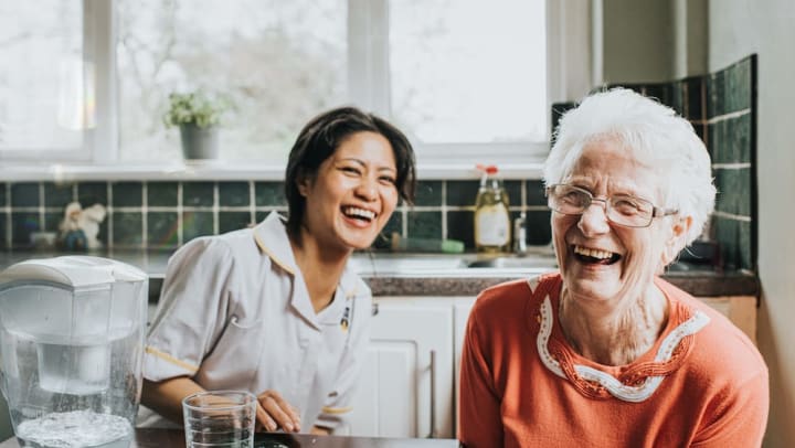 Elderly woman and young nurse smiling and laughing in a kitchen