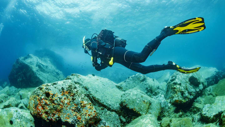 A person scuba dives over rocks in the ocean