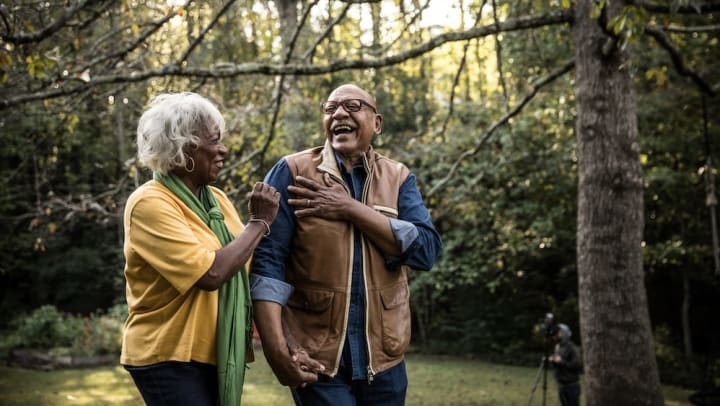 Older man and older woman talking and laughing outside by a tree