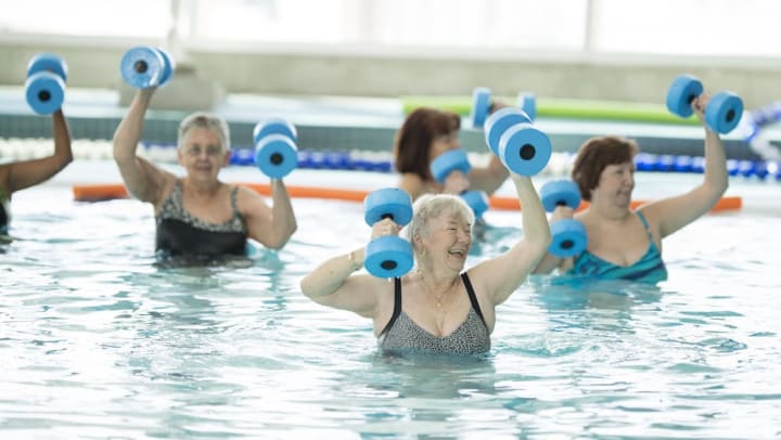Several older women in an indoor pool lifting foam weights