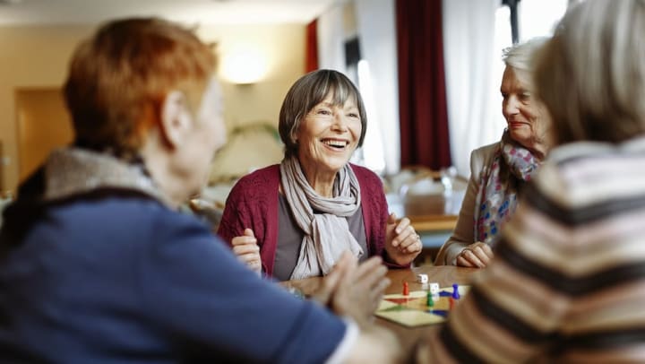Four older women smiling and sitting at a table while playing a board game