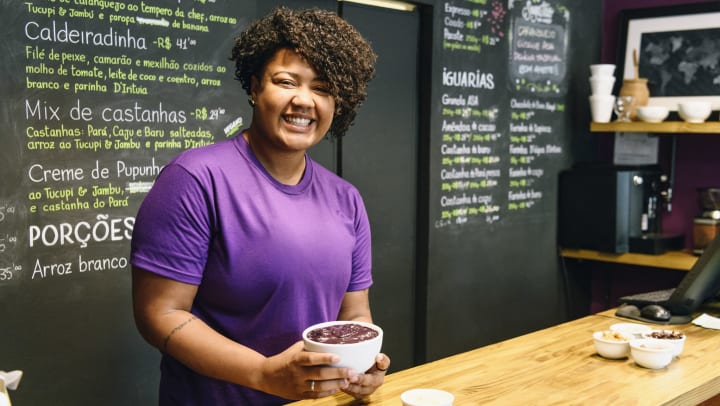 Woman in a purple shirt holding an acai bowl behind a counter. 