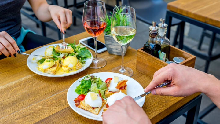 Two plates of eggs benedict and two glasses of wine sitting on a wooden table