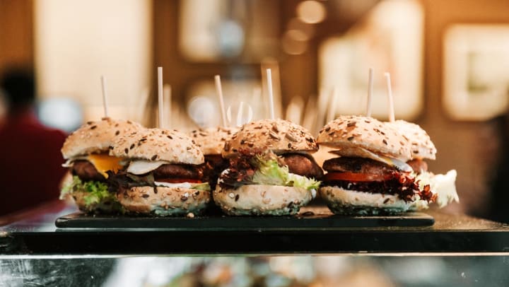 Assorted cheeseburger sliders with lettuce and tomato on a black tray | Sliders Near Keller
