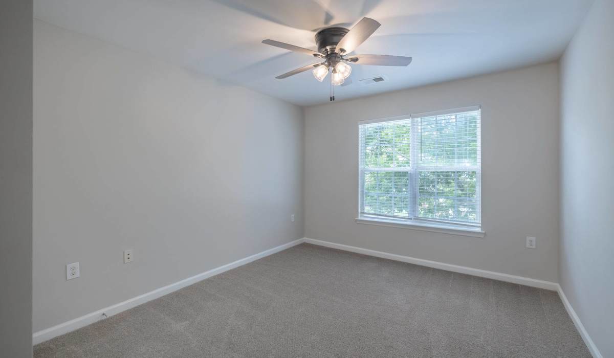 Unfurnished bedroom with ceiling fan, large window and carpet flooring at Palisades at Carters Mill in Sumter, South Carolina