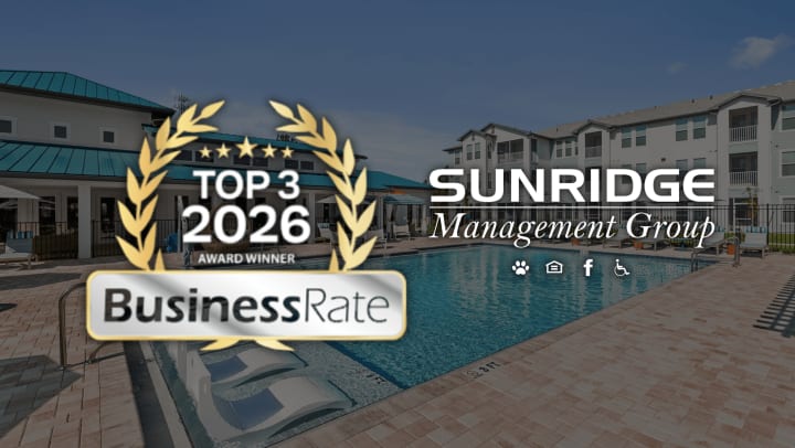 A modern apartment community pool with lounge chairs and surrounding buildings, overlaid with a gold “Top 3 2026 Award Winner” badge from BusinessRate and the SunRidge Management Group logo.