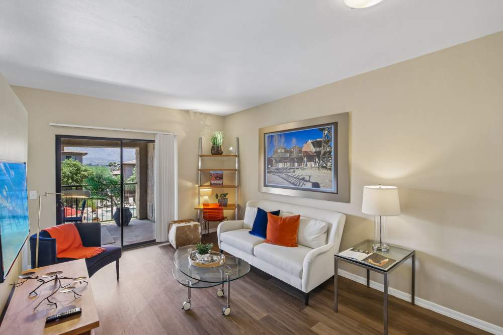 Living room with sliding glass door, white sectional sofa, and orange throw pillows at Oro Vista Apartments in Oro Valley, Arizona