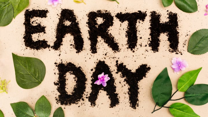 Top view of Earth Day lettering with leaves and buds on beige background.