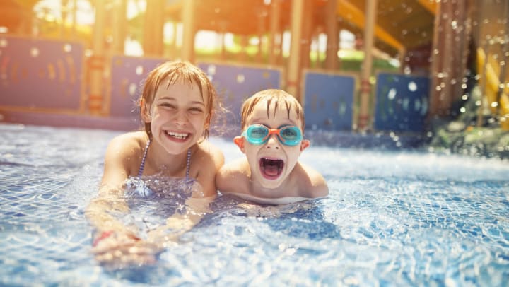 Little girl and her brother are smiling while lying in shallow water in a water park.