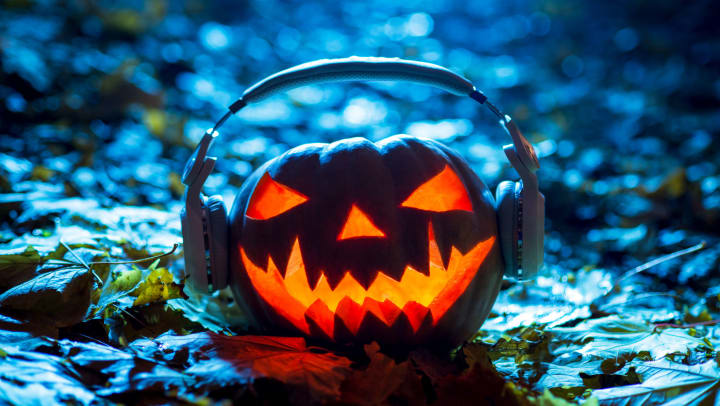 Jack-o-lantern sitting in leaves wearing a pair of headphones