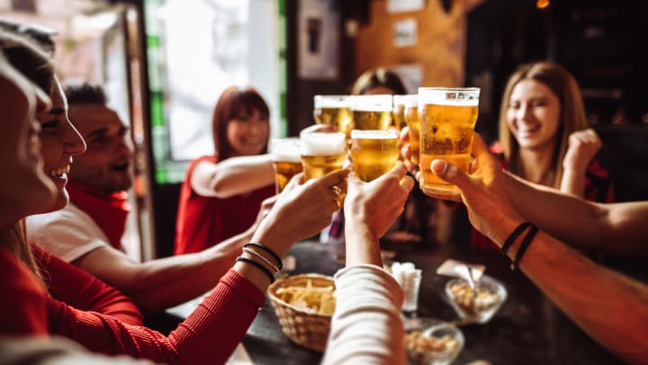 A group of people sitting around a table toasting beer glasses together.