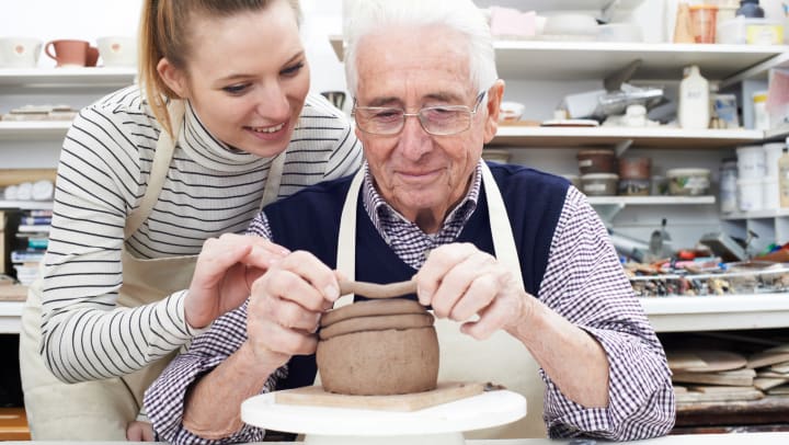 A senior and caregiver work on pottery