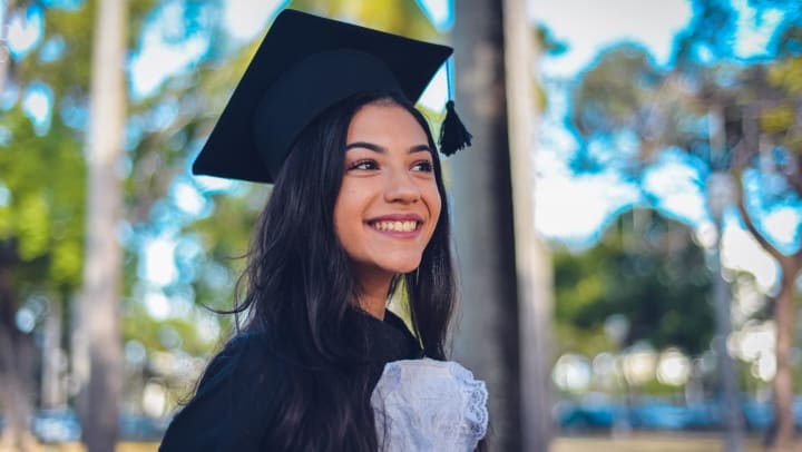 A smiling young woman wearing a graduation cap and gown.