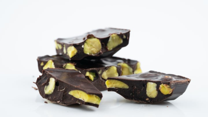 Dark chocolate pieces with pistachio inside against a white backdrop.