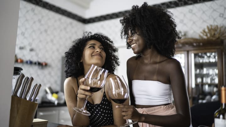 Two women looking at each other and smiling while they clink wine glasses