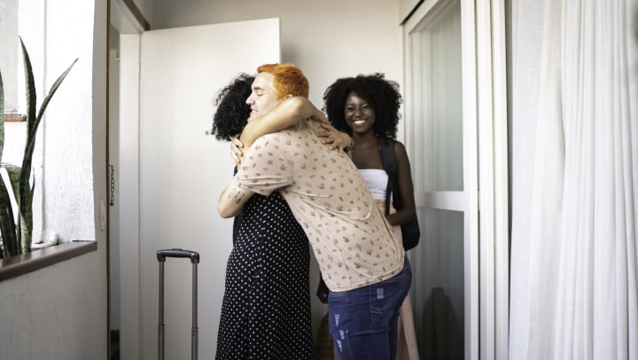 A friend acting as a host welcomes guests into home with hugs.